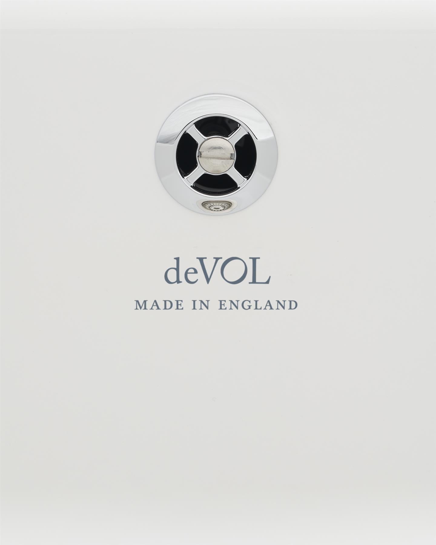 A close-up view of a circular sink overflow cap in a polished chrome finish fitted to a ceramic sink. A logo on the ceramic sink below reads 'deVOL; Made in England'.