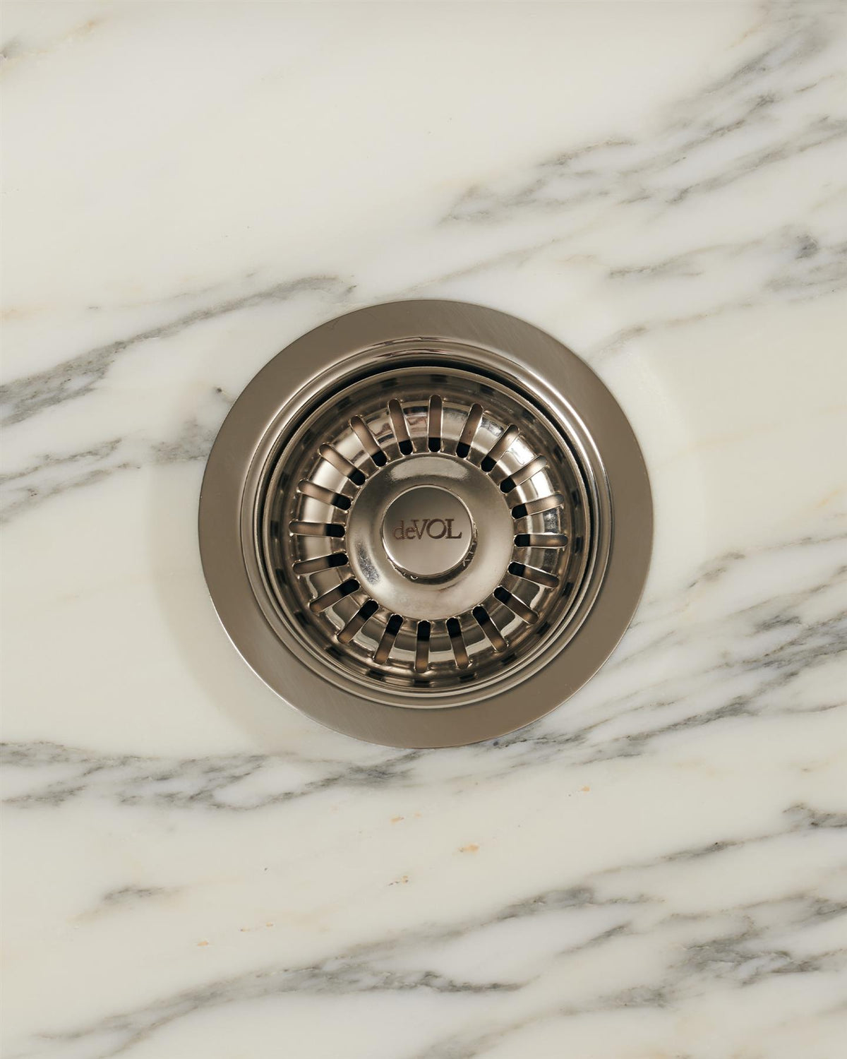 An overhead view of a basket waste strainer in a polished chrome finish, there is a small 'deVOL' logo in the middle of the central finial. TEST
