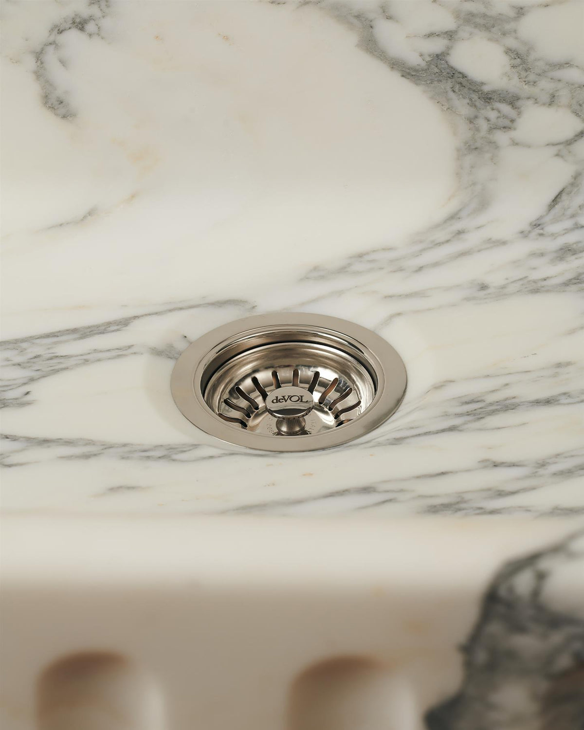 A straight-on view of a basket waste strainer in a polished chrome finish fitted in an Arabescato marble sink. TEST
