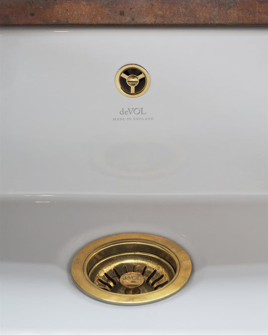 A straight-on view of a basket waste strainer with a standard round overflow cap in a warm burnished brass finish, there is a small 'deVOL' logo in the middle of the waste strainer finial.