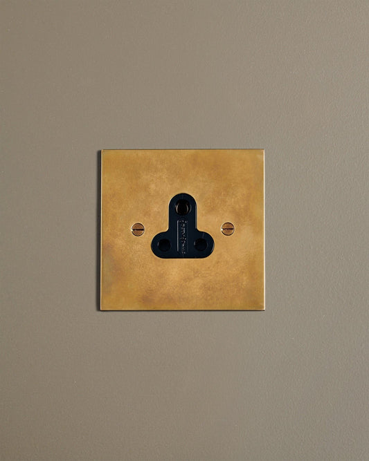 A straight-on view of a classic 5 amp single plug socket in a warm burnished brass finish.