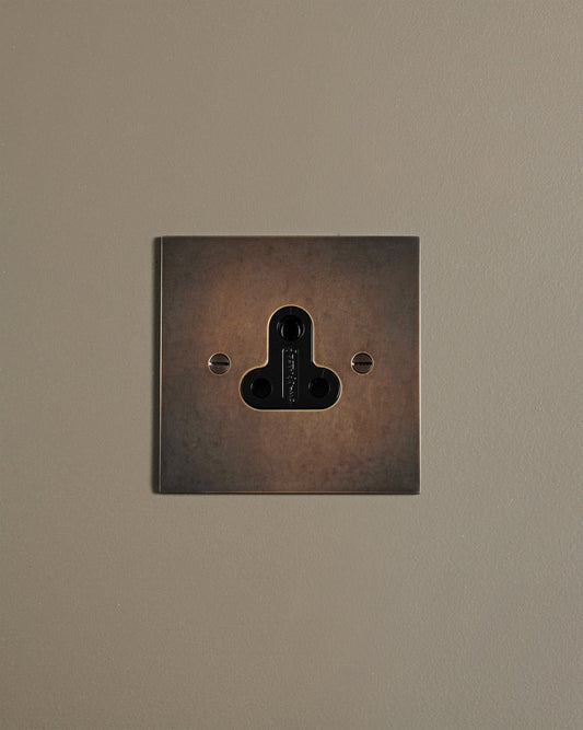 A straight-on view of a classic 5 amp single plug socket in a dark oxidised brass finish.