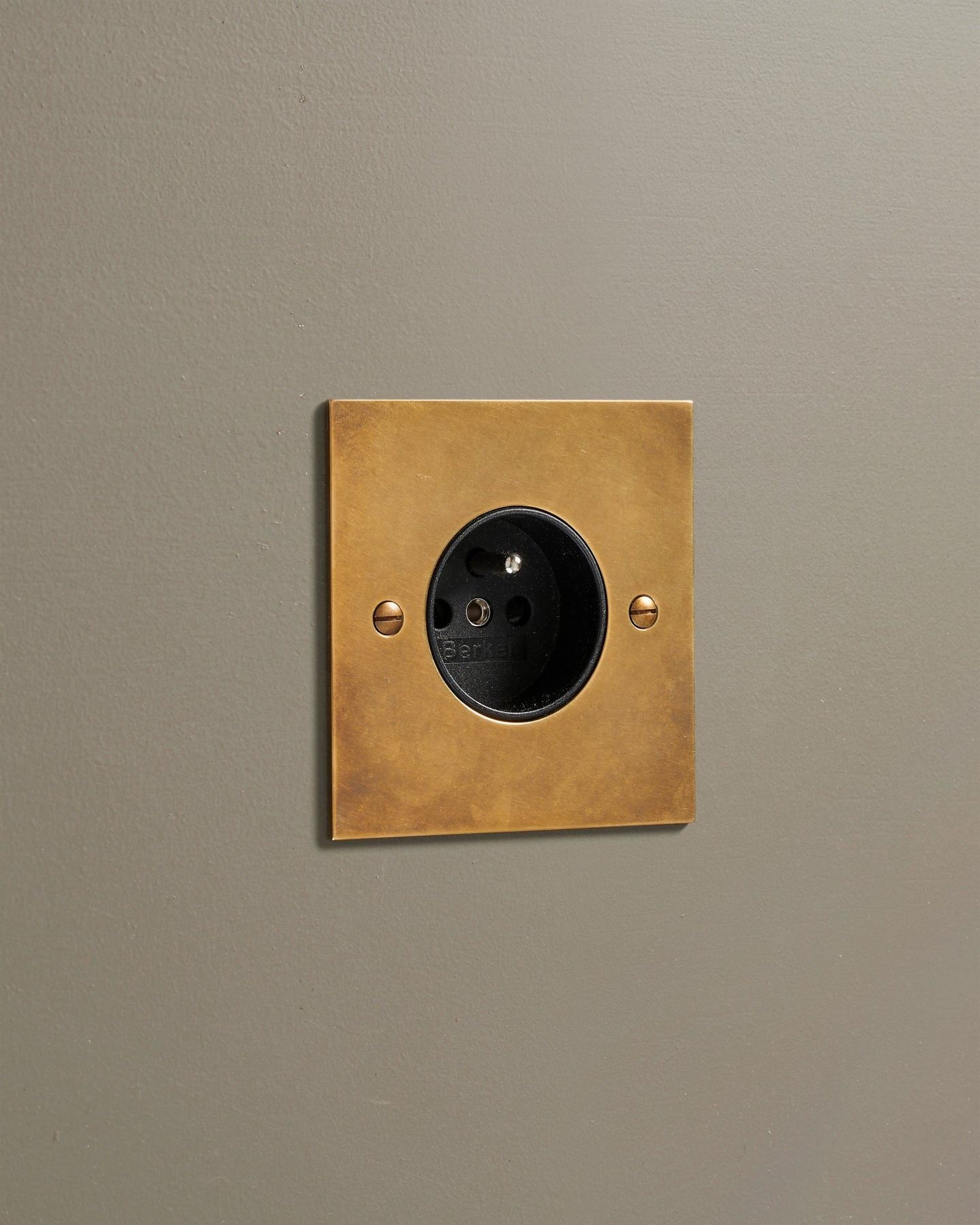 A straight-on view of a classic French-style single plug socket in a warm burnished brass finish.