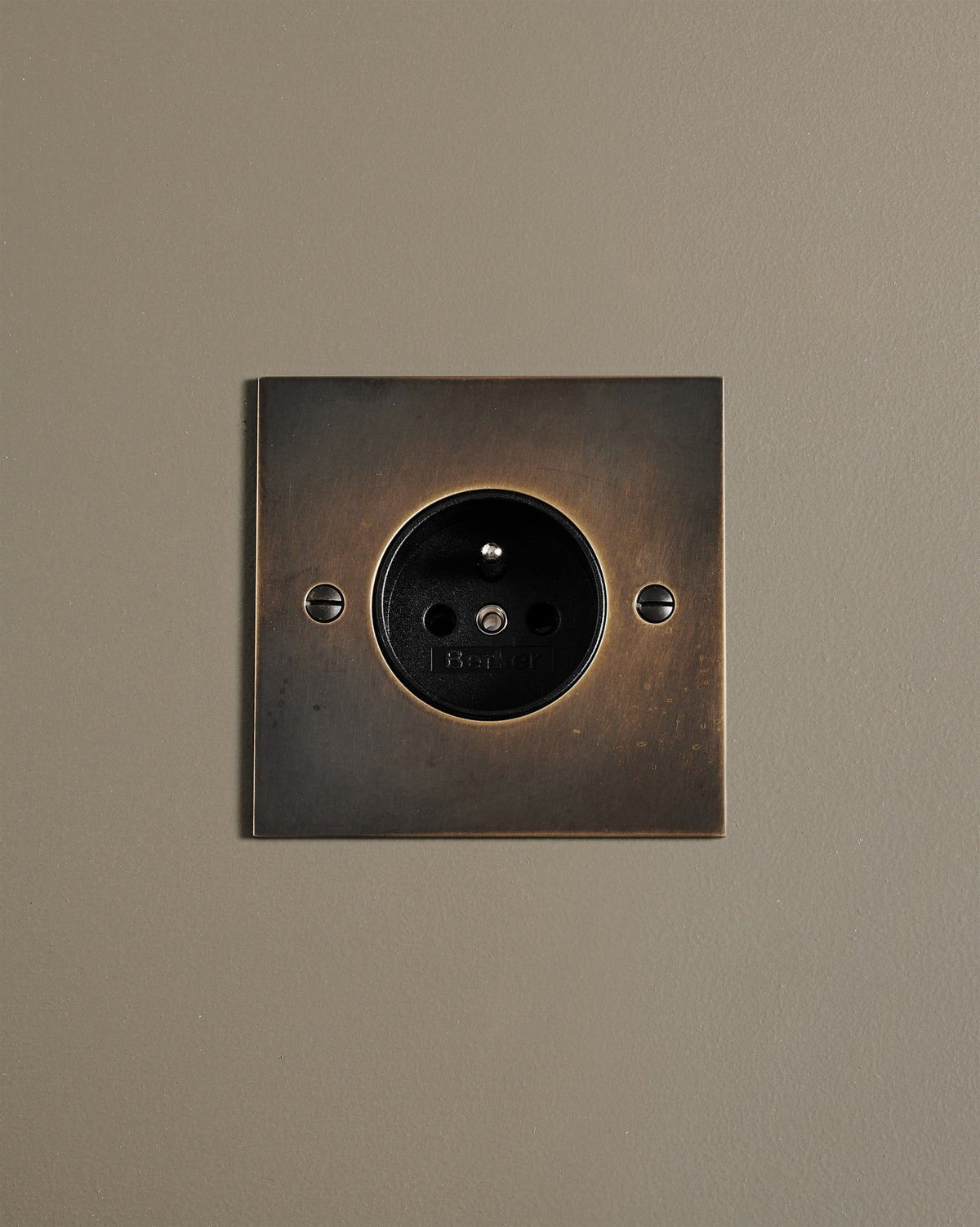 A straight-on view of a classic French-style single plug socket in a dark oxidised brass finish. TEST