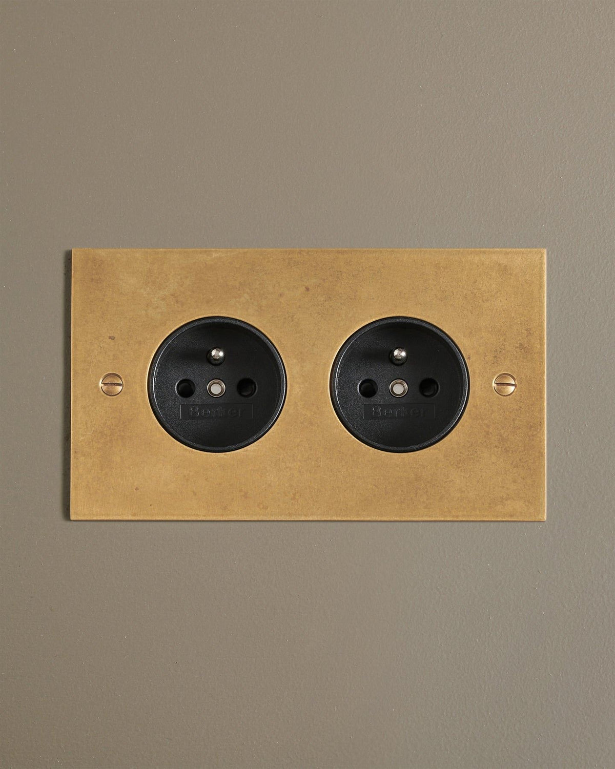 A straight-on view of a classic French-style twin plug socket in a mottled aged brass finish. TEST