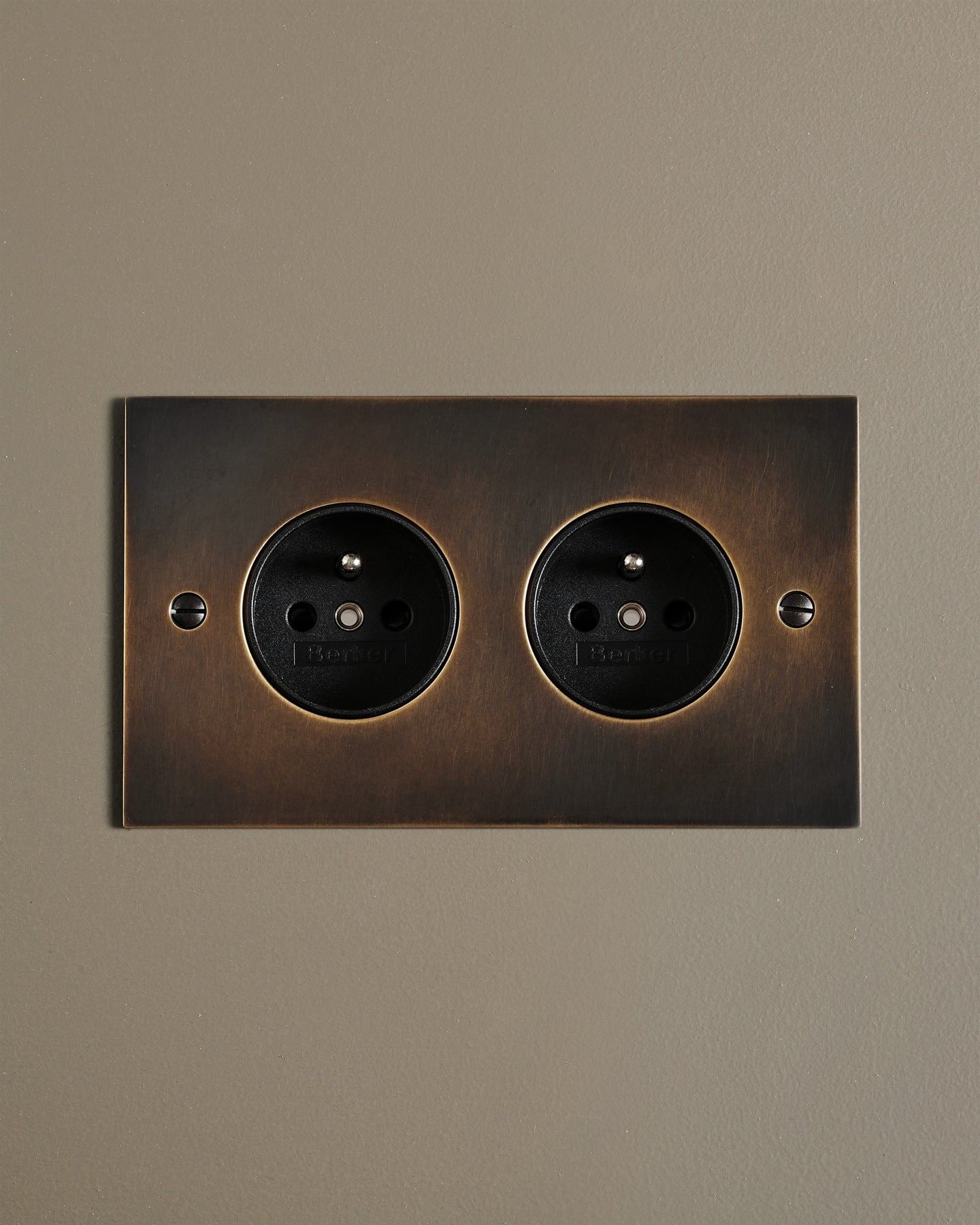 A straight-on view of a classic French-style twin plug socket in a dark oxidised brass finish.