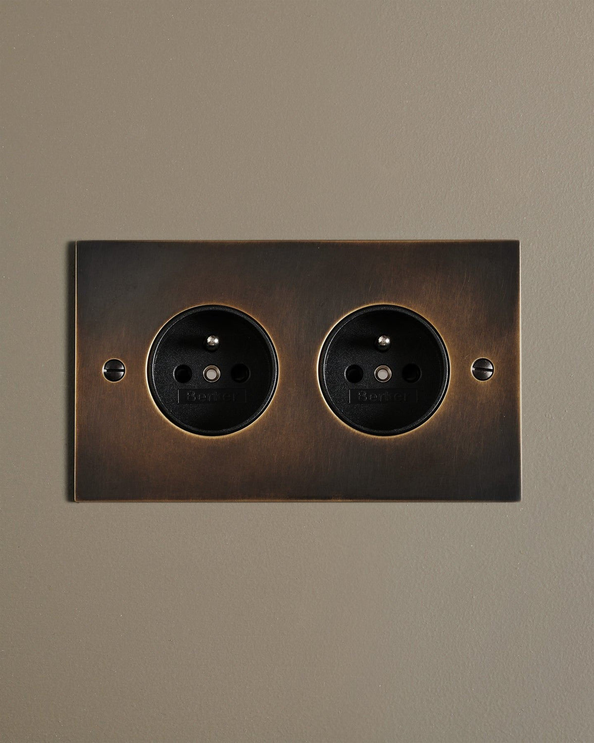 A straight-on view of a classic French-style twin plug socket in a dark oxidised brass finish. TEST