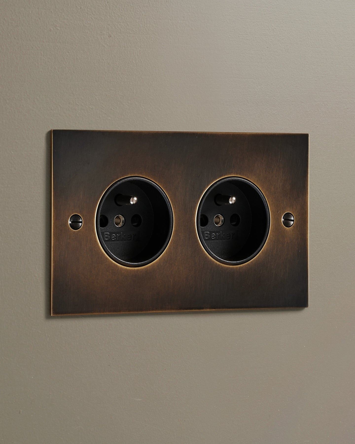 An oblique view of a classic French-style twin plug socket in a dark oxidised brass finish.