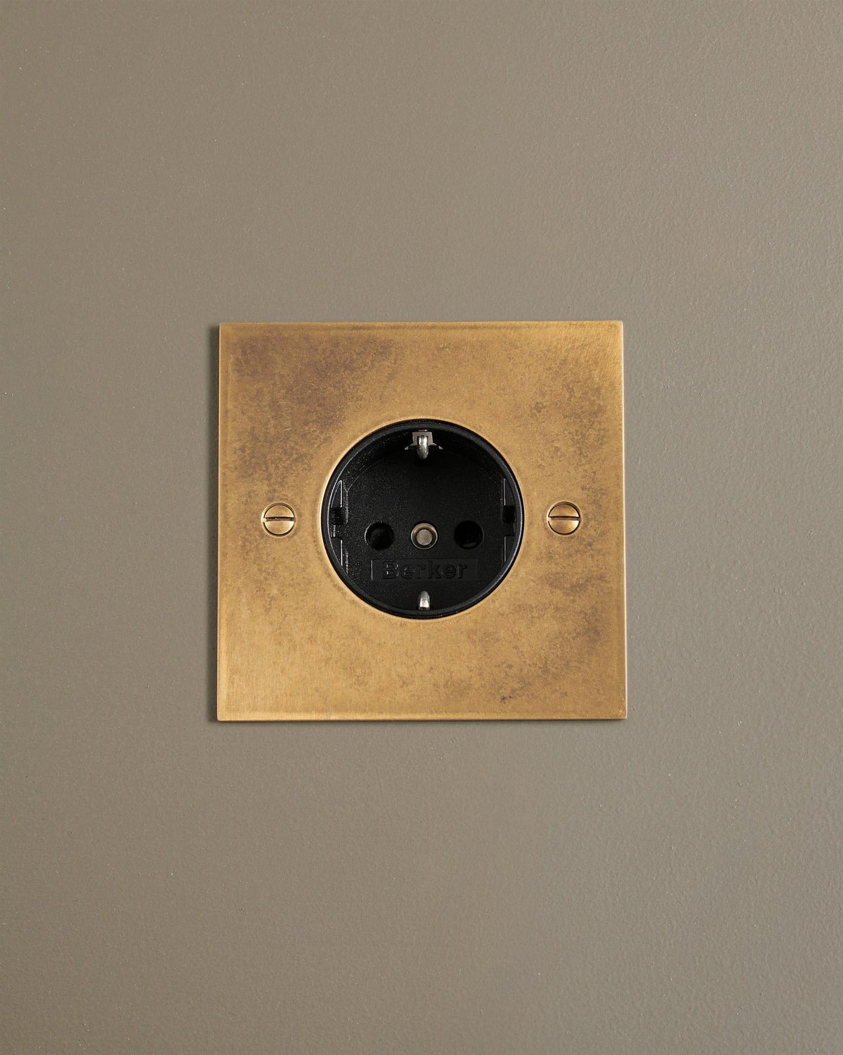 A straight-on view of a classic Schuko-style single plug socket in a mottled aged brass finish. TEST