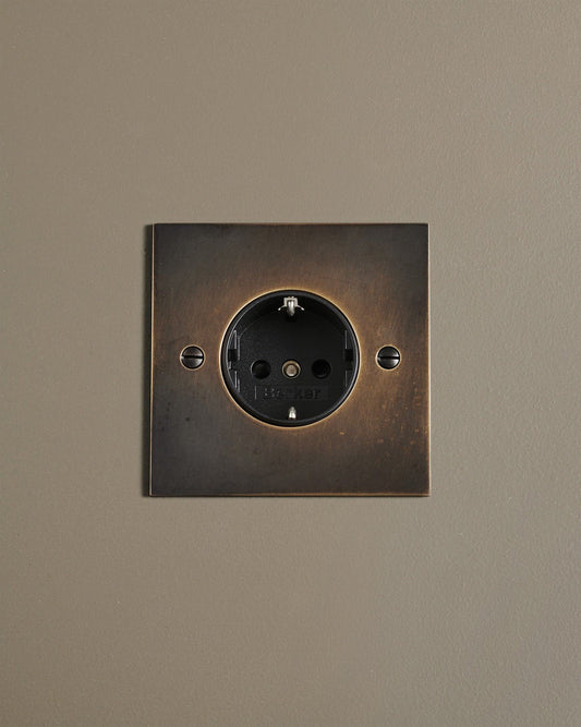 A straight-on view of a classic Schuko-style single plug socket in a dark oxidised brass finish.