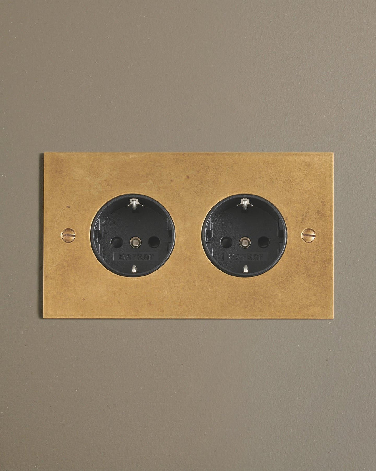 A straight-on view of a classic Schuko-style twin plug socket in a mottled aged brass finish. TEST