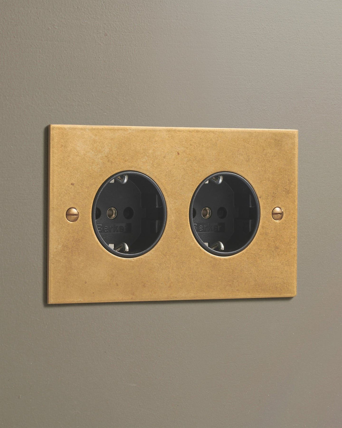 An oblique view of a classic Schuko-style twin plug socket in a mottled aged brass finish. TEST