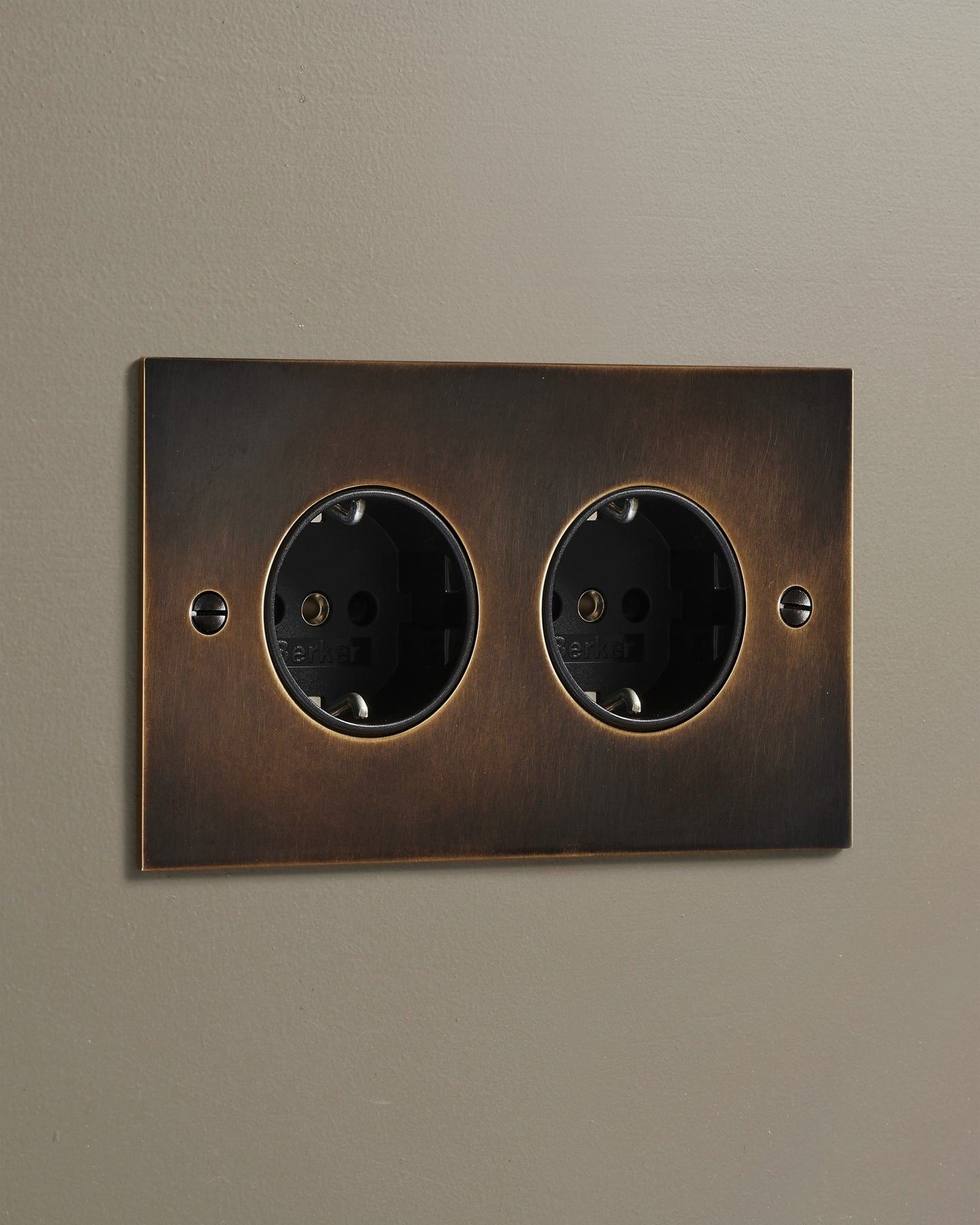 An oblique view of a classic Schuko-style twin plug socket in a dark oxidised brass finish.