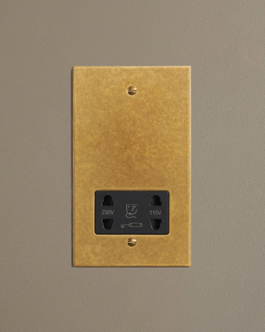 A straight-on view of a classic twin shaver socket in a mottled aged brass finish.