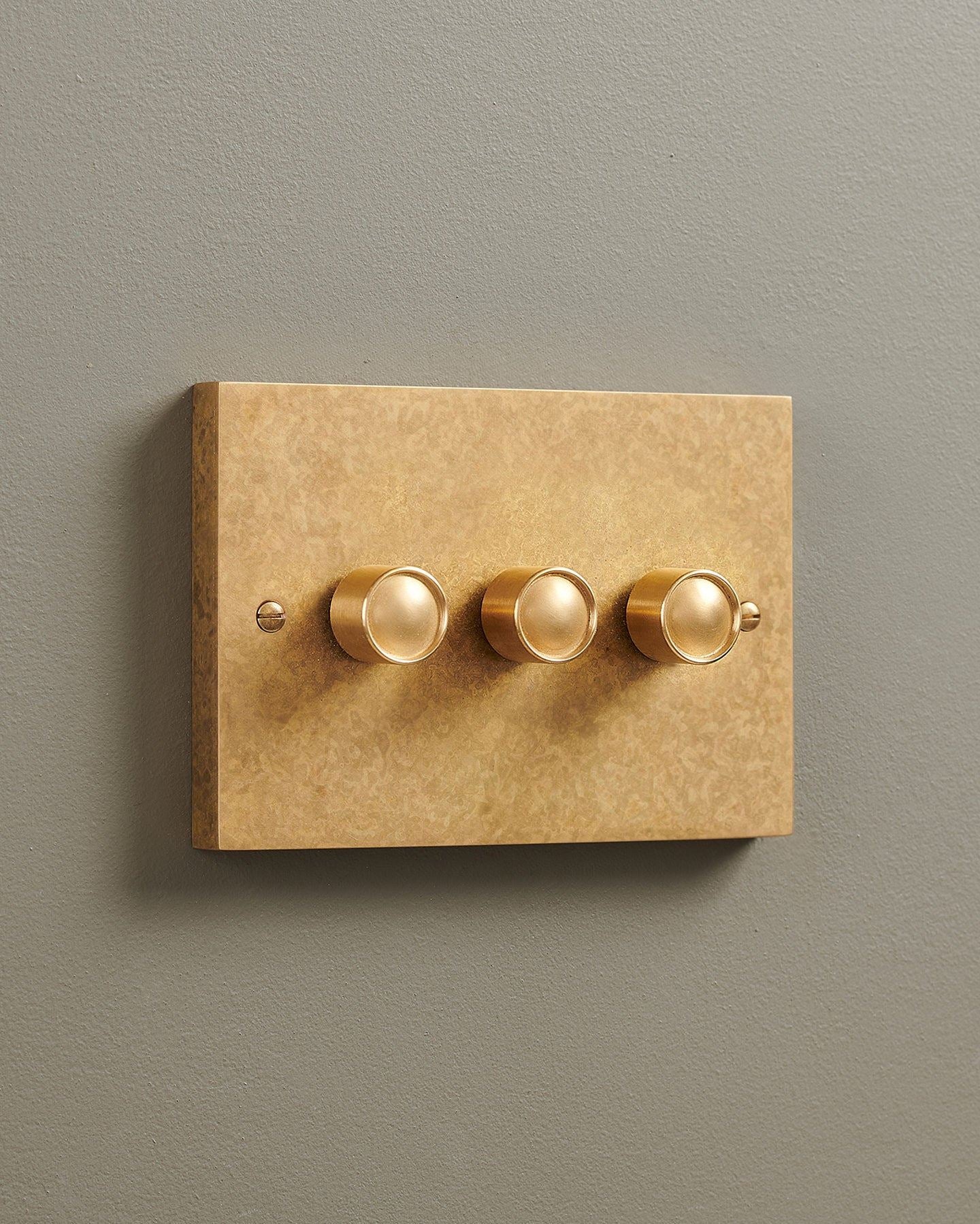 An oblique view of a 3 gang box dimmer switch in a mottled aged brass finish.