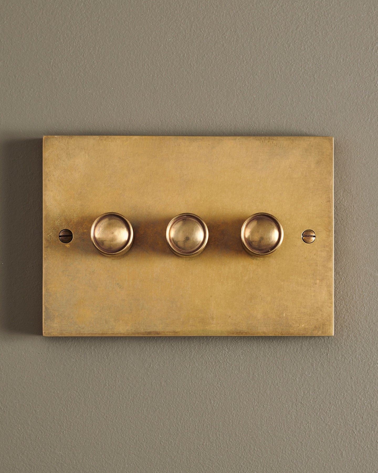 A straight-on view of a 3 gang box dimmer switch in a warm burnished brass finish.