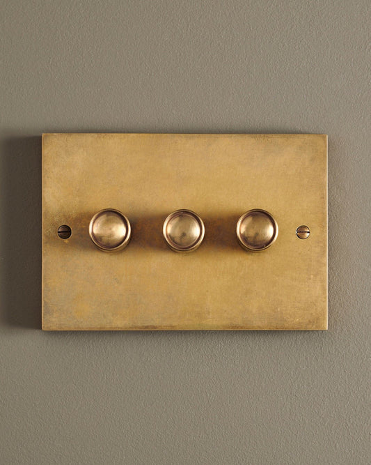 A straight-on view of a 3 gang box dimmer switch in a warm burnished brass finish.