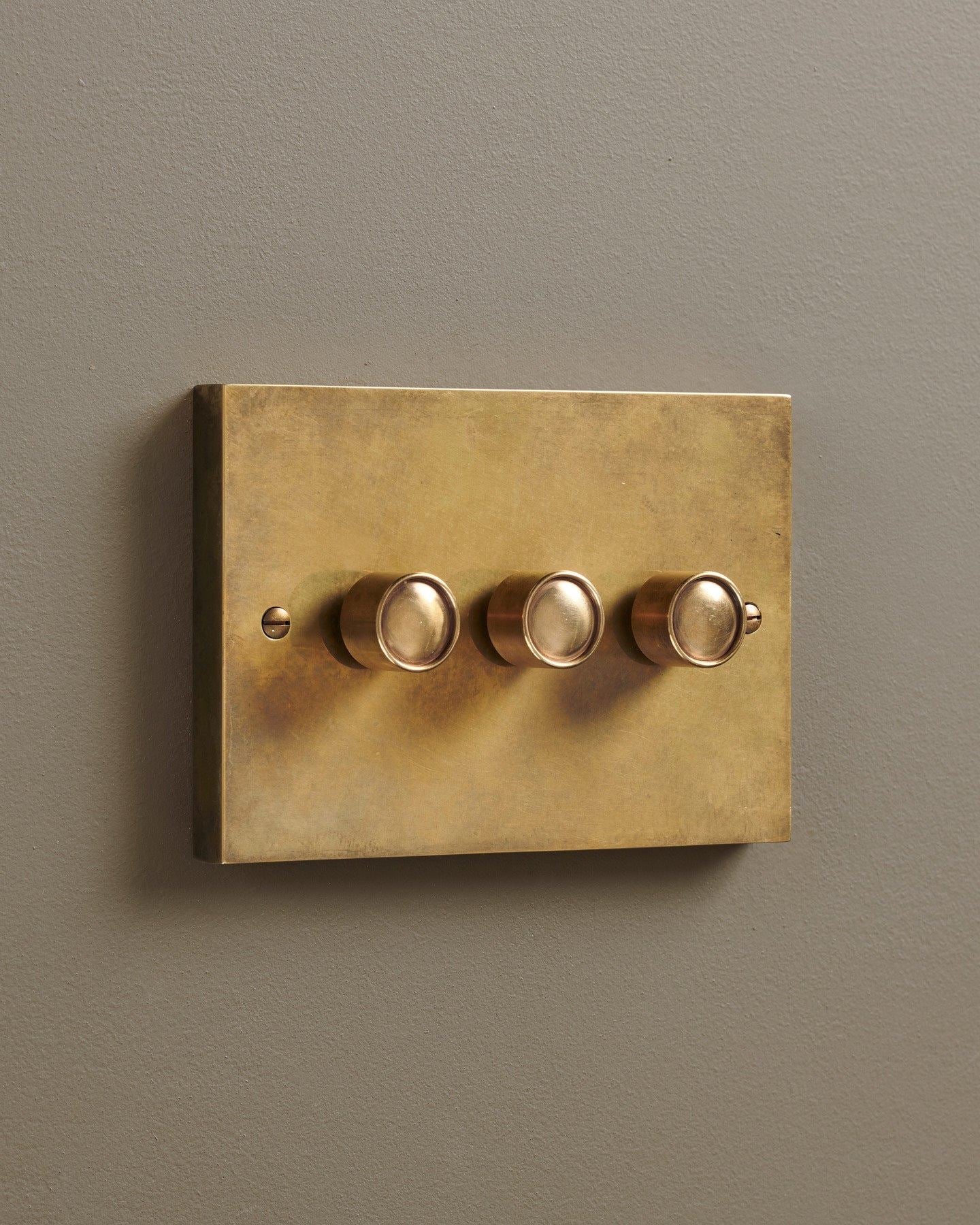 An oblique view of a 3 gang box dimmer switch in a warm burnished brass finish.