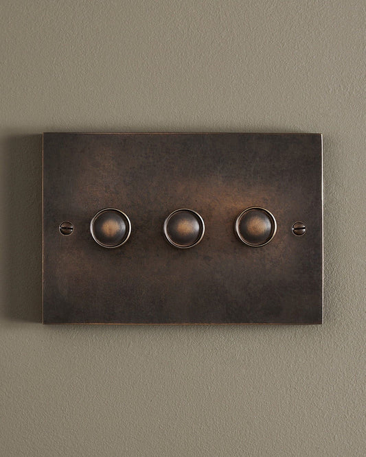 A straight-on view of a 3 gang box dimmer switch in a dark oxidised brass finish.