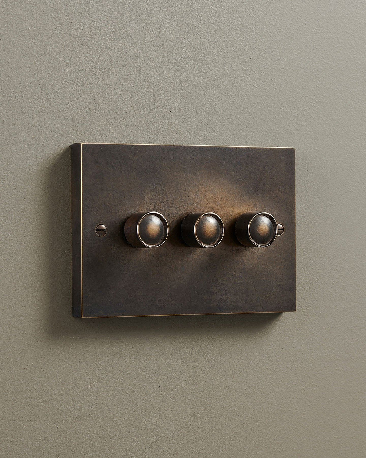 An oblique view of a 3 gang box dimmer switch in a dark oxidised brass finish. TEST