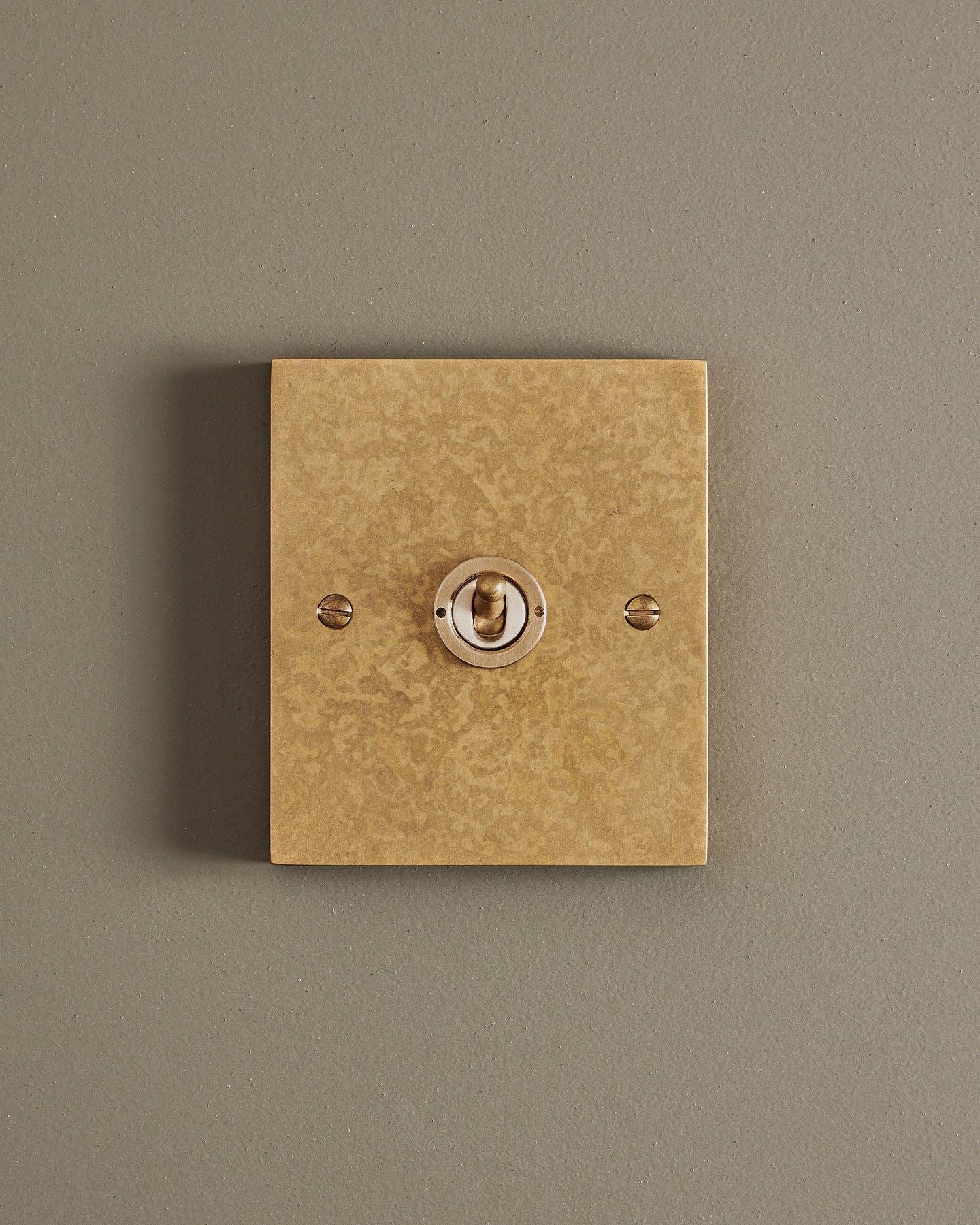 A straight-on view of a 1 gang box toggle switch in a mottled aged brass finish.