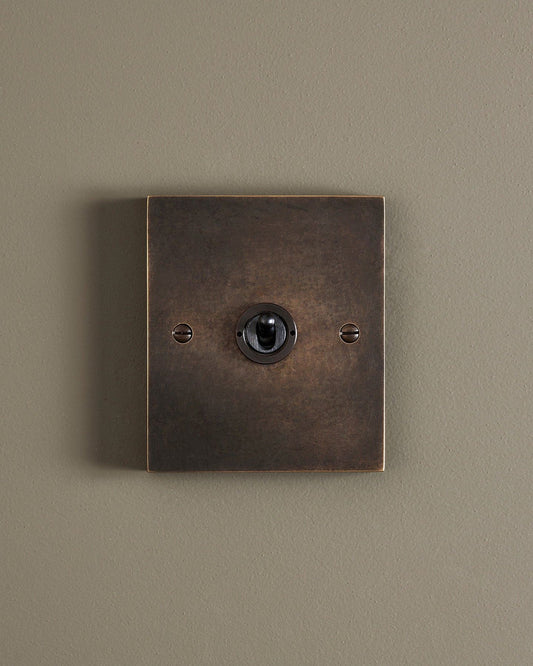 A straight-on view of a 1 gang box toggle switch in a dark oxidised brass finish.
