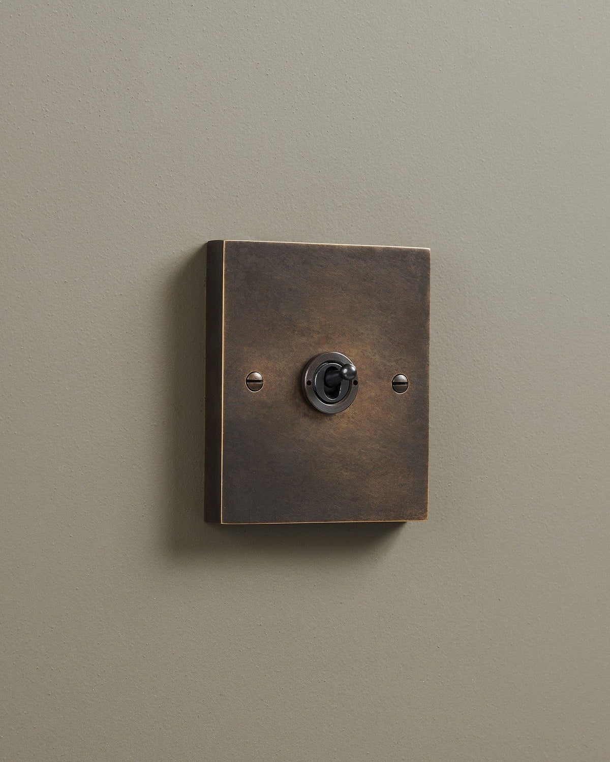 An oblique view of a 1 gang box toggle switch in a dark oxidised brass finish. TEST