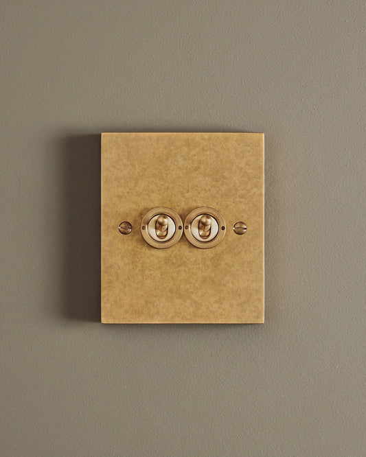 A straight-on view of a 2 gang box toggle switch in a mottled aged brass finish.