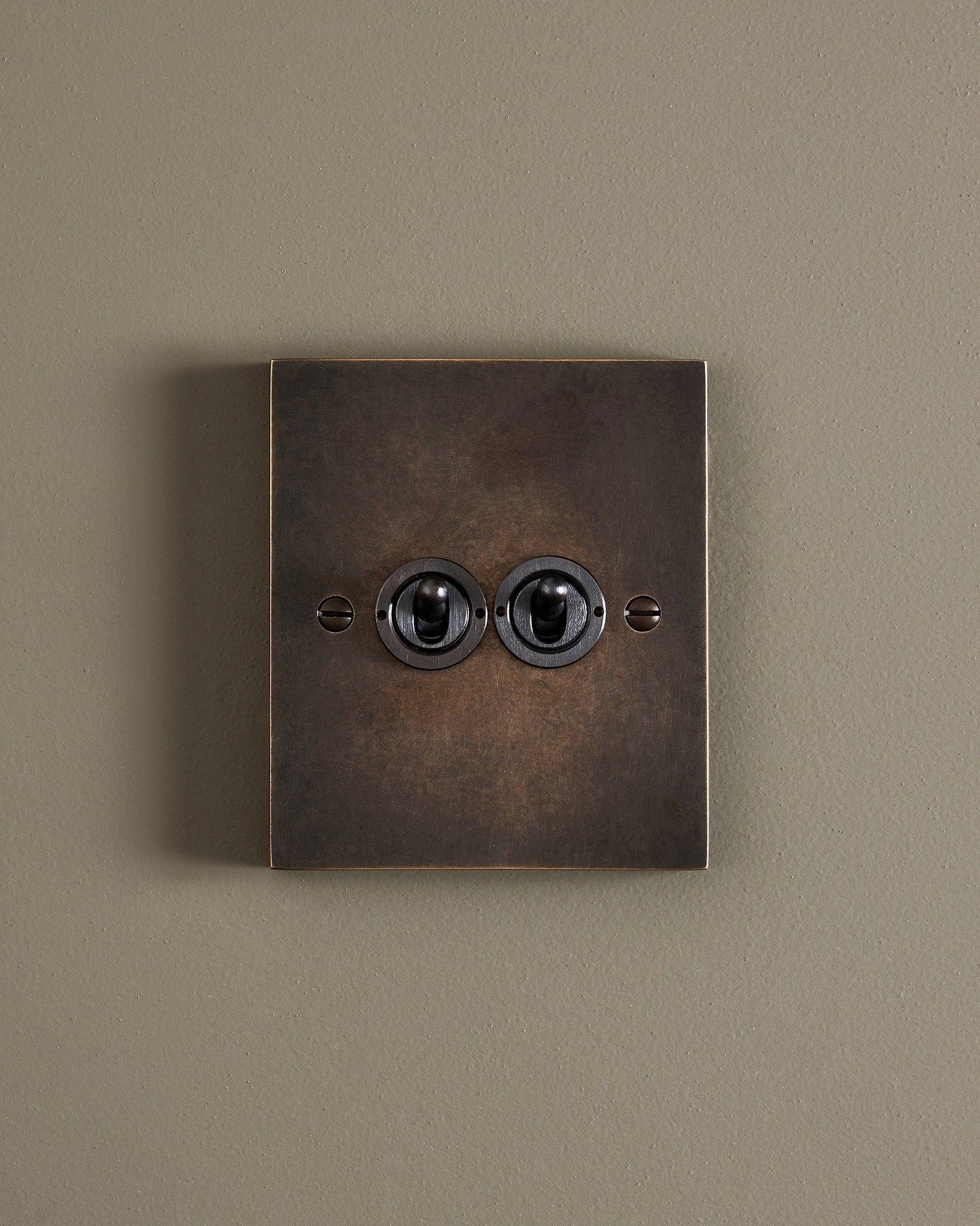 A straight-on view of a 2 gang box toggle switch in a dark oxidised brass finish.