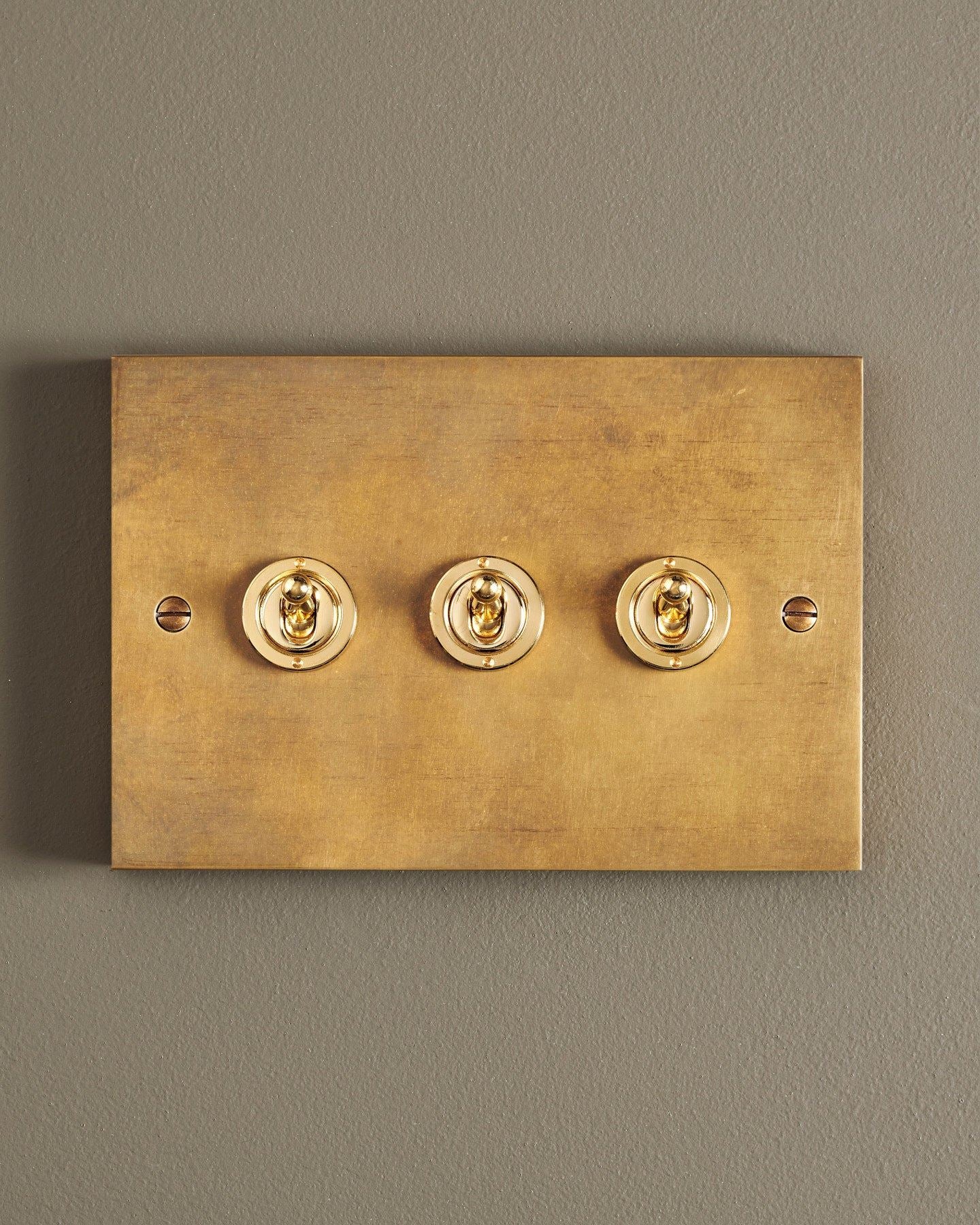A straight-on view of a 3 gang box toggle switch in a warm burnished brass finish.