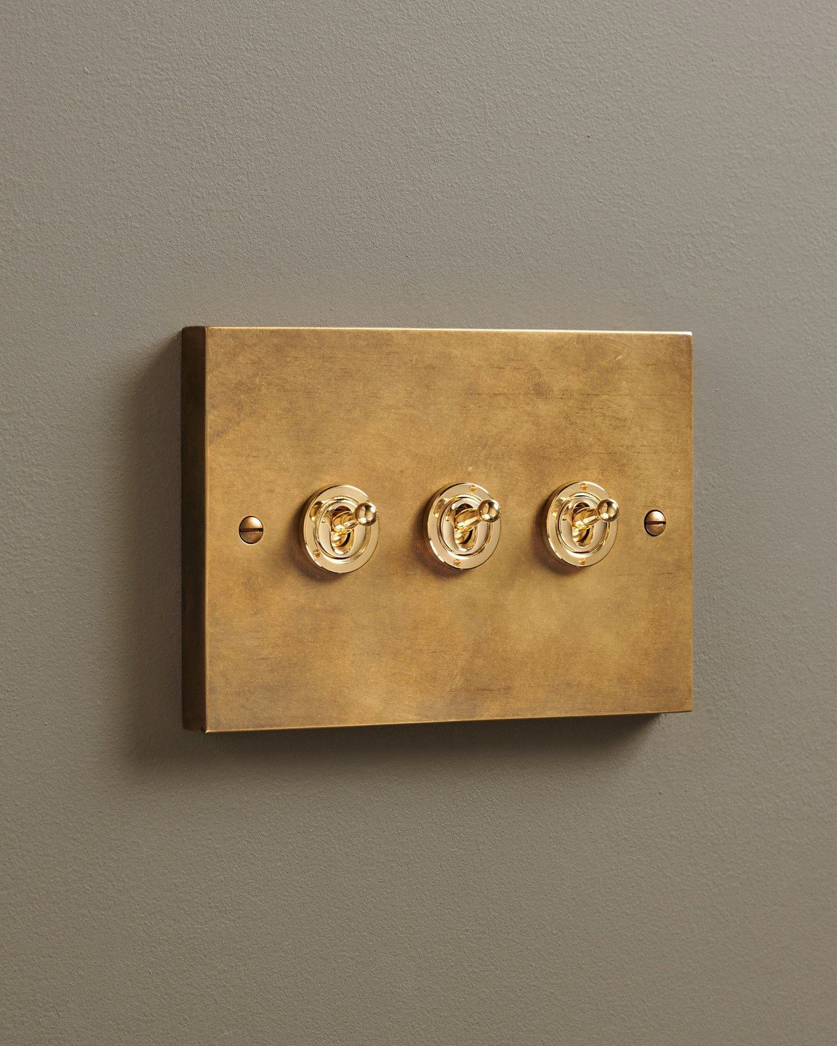 An oblique view of a 3 gang box toggle switch in a warm burnished brass finish. TEST