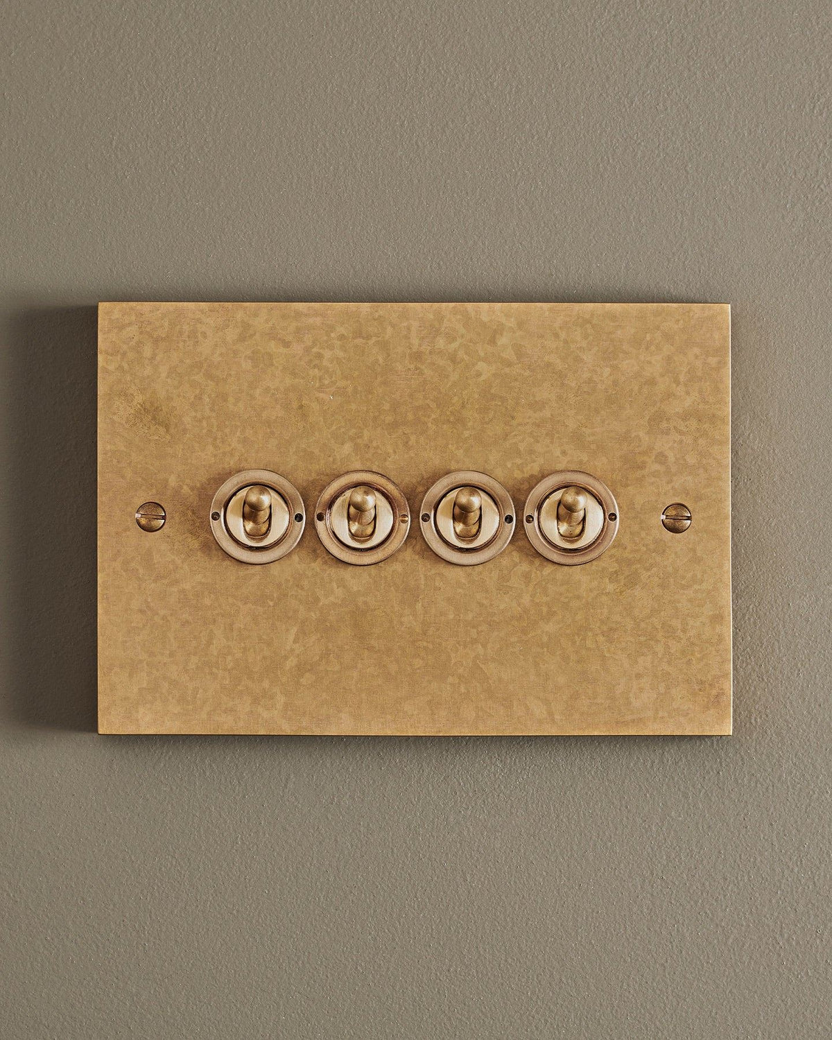 A straight-on view of a 4 gang box toggle switch in a mottled aged brass finish. TEST