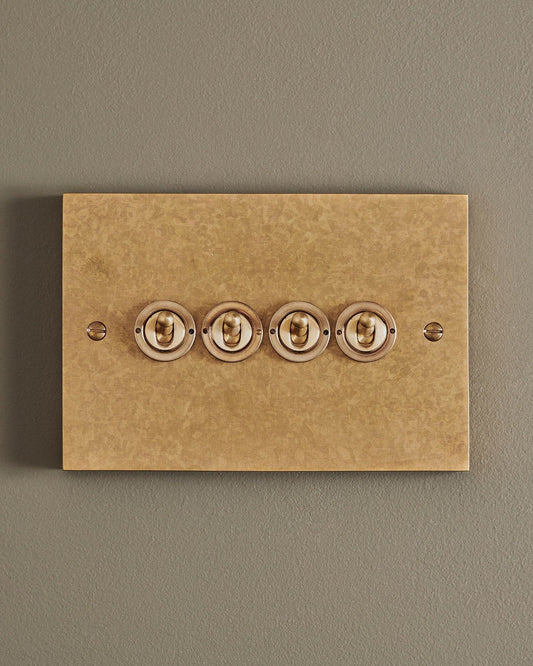 A straight-on view of a 4 gang box toggle switch in a mottled aged brass finish.