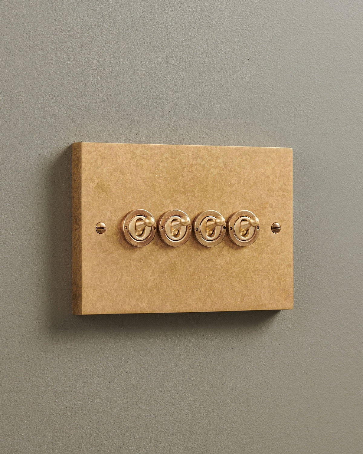 An oblique view of a 4 gang box toggle switch in a mottled aged brass finish. TEST