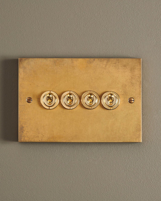 A straight-on view of a 4 gang box toggle switch in a warm burnished brass finish.