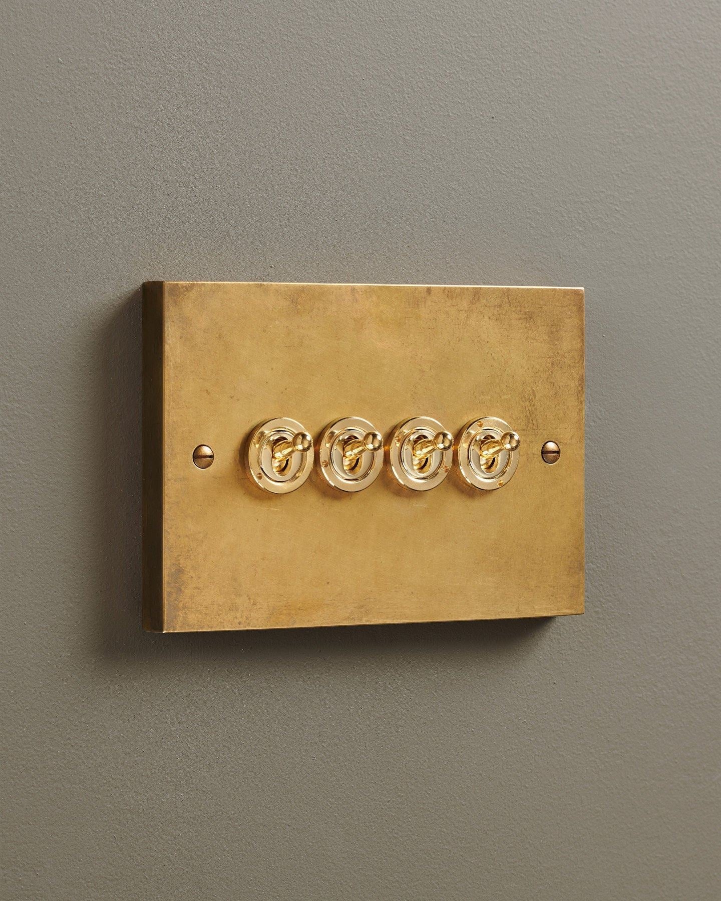 An oblique view of a 4 gang box toggle switch in a warm burnished brass finish.