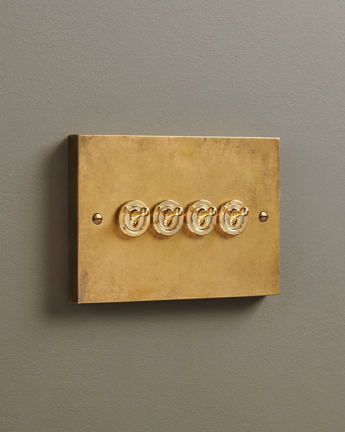 An oblique view of a 4 gang box toggle switch in a warm burnished brass finish. TEST