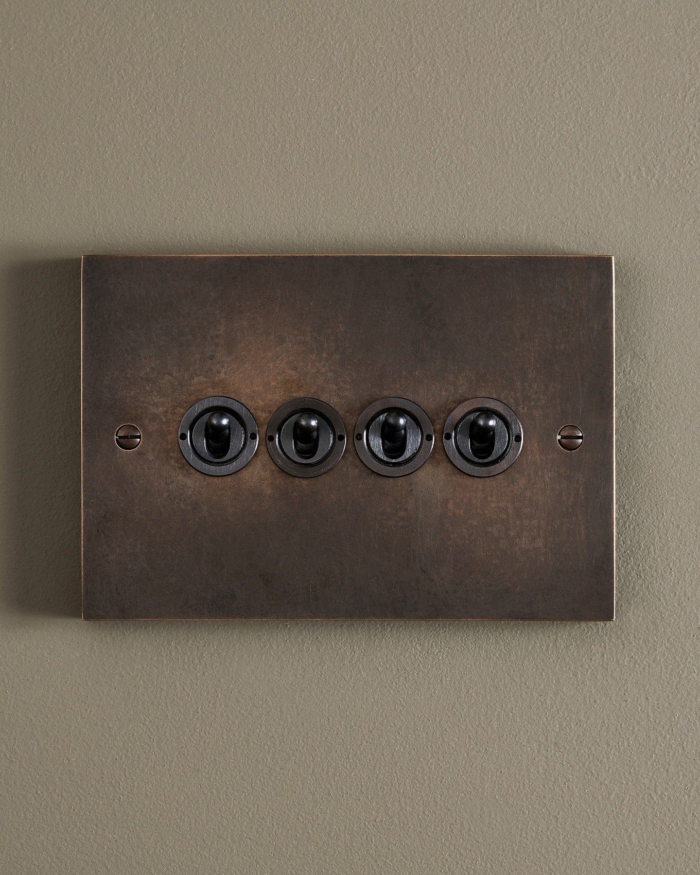 A straight-on view of a 4 gang box toggle switch in a dark oxidised brass finish.