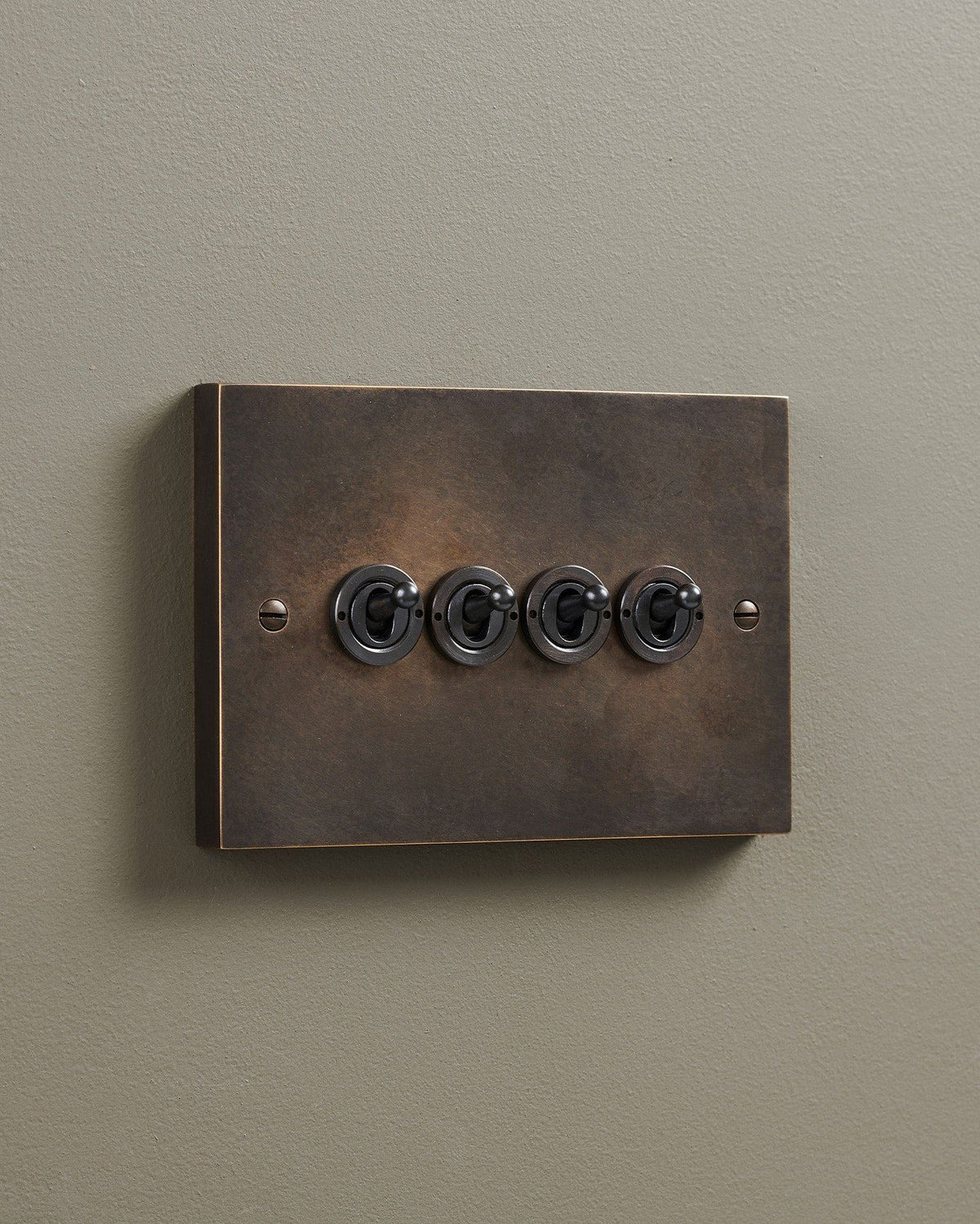 An oblique view of a 4 gang box toggle switch in a dark oxidised brass finish. TEST