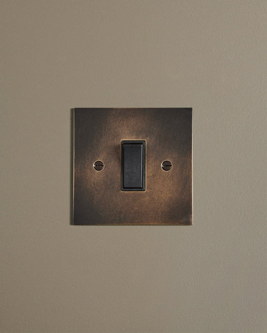 A straight-on view of a classic 20 amp switch in a dark oxidised brass finish.