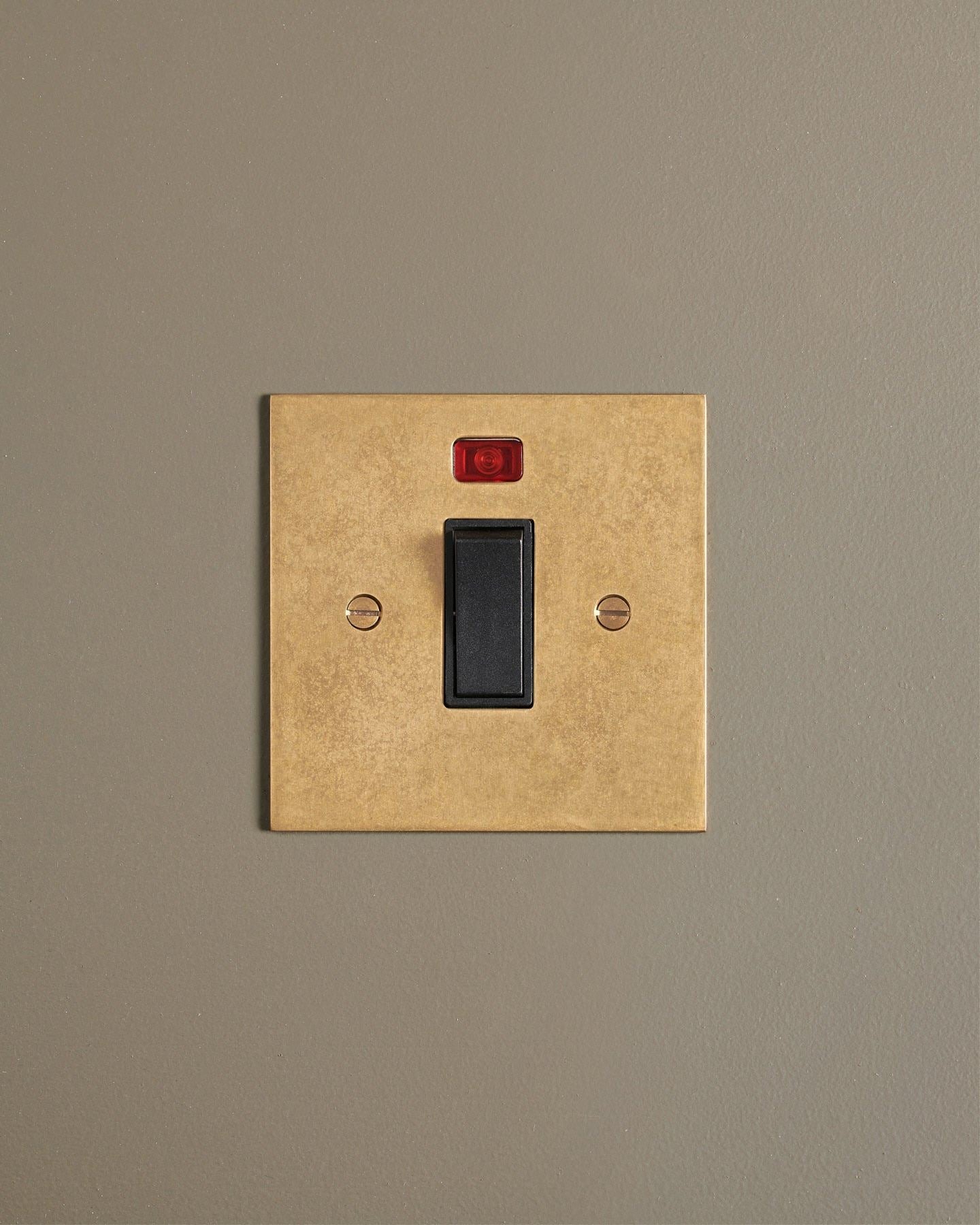 A straight-on view of a classic 32 amp cooker switch in a mottled aged brass finish.