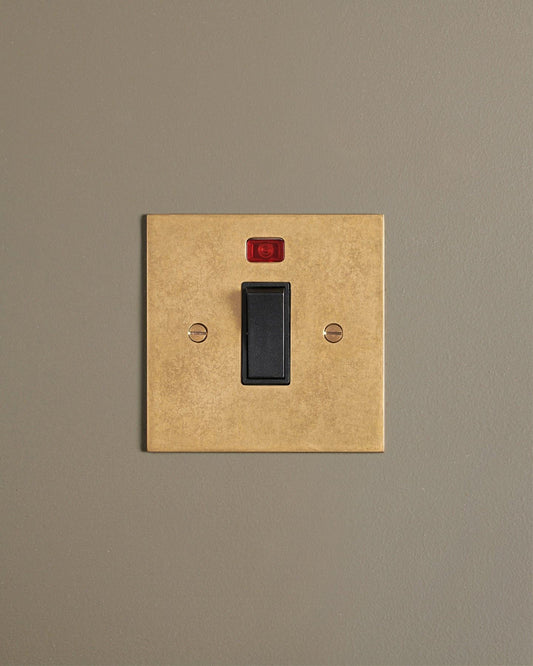 A straight-on view of a classic 32 amp cooker switch in a mottled aged brass finish.