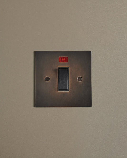 A straight-on view of a classic 32 amp cooker switch in a dark oxidised brass finish.