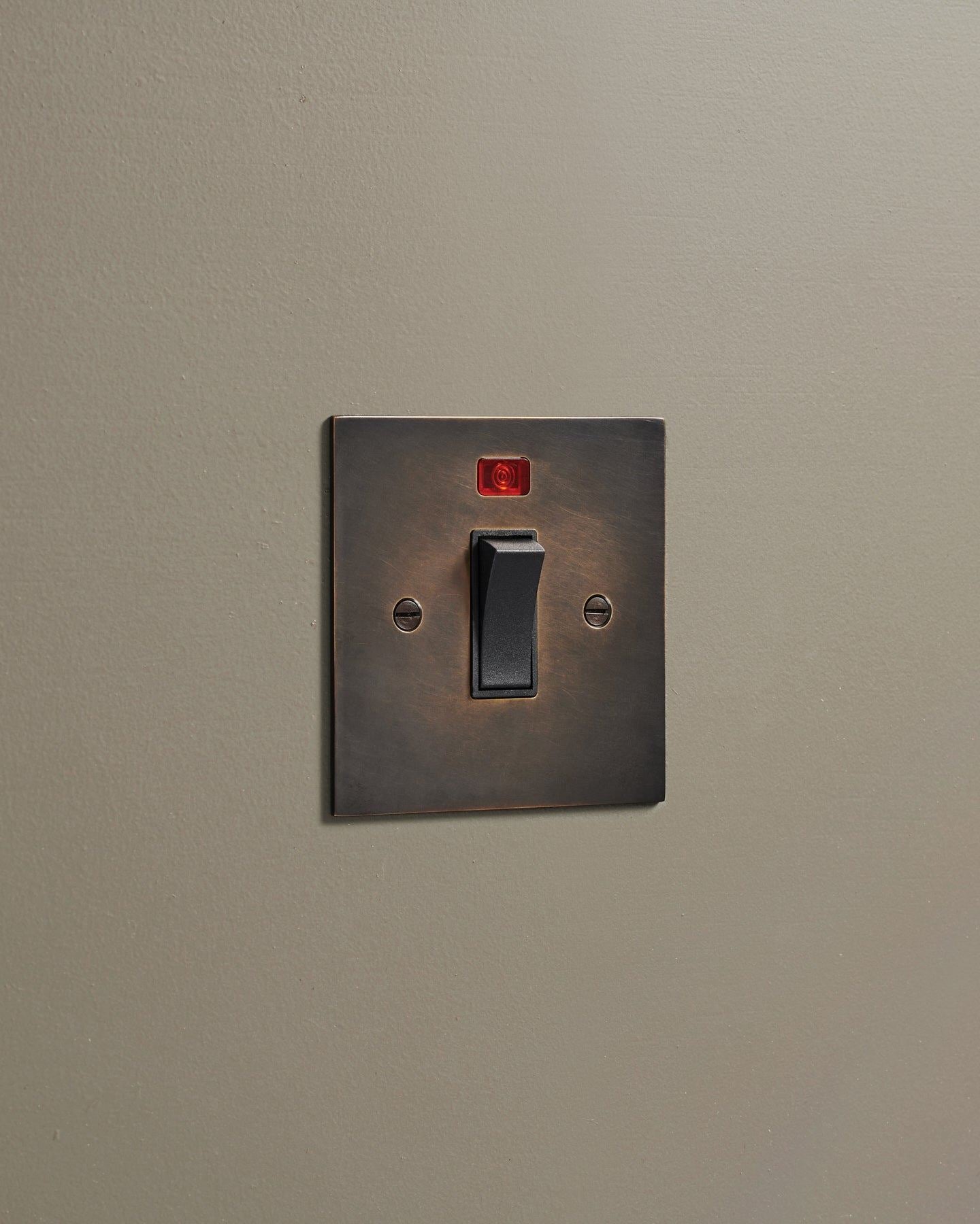 An oblique view of a classic 32 amp cooker switch in a dark oxidised brass finish.