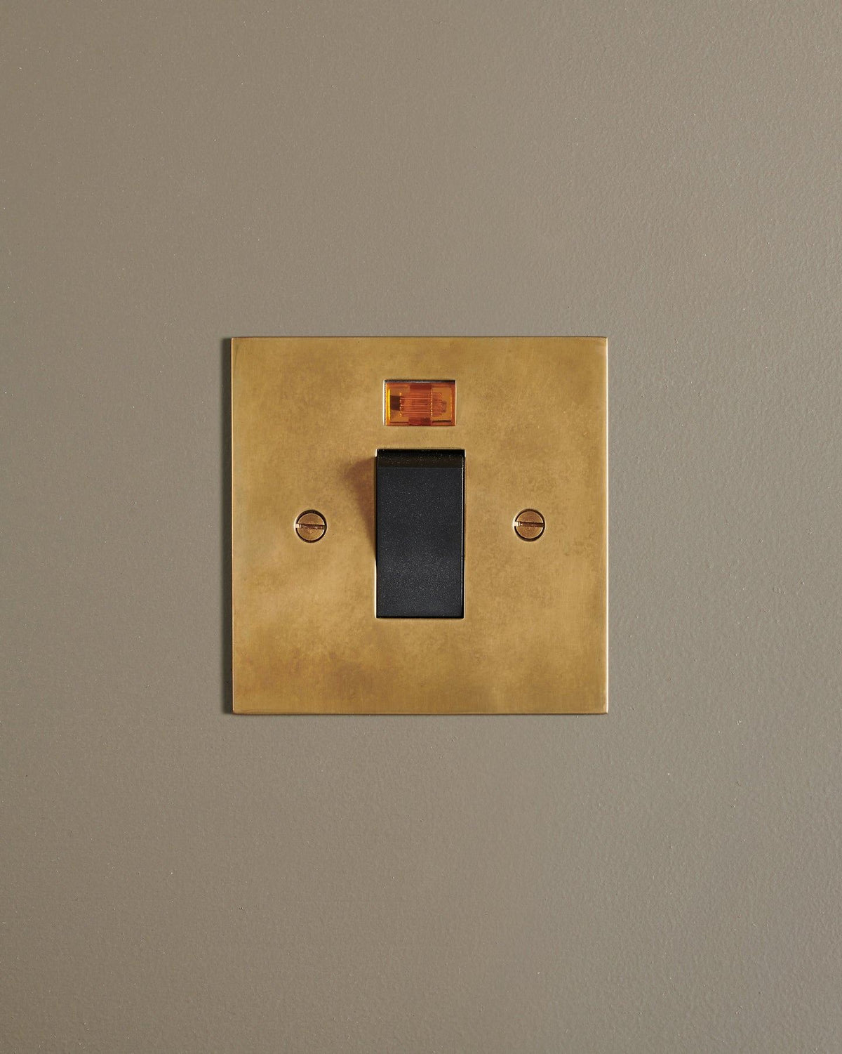 A straight-on view of a classic 45 amp cooker switch in a warm burnished brass finish. TEST