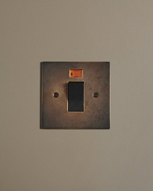 A straight-on view of a classic 45 amp cooker switch in a dark oxidised brass finish.