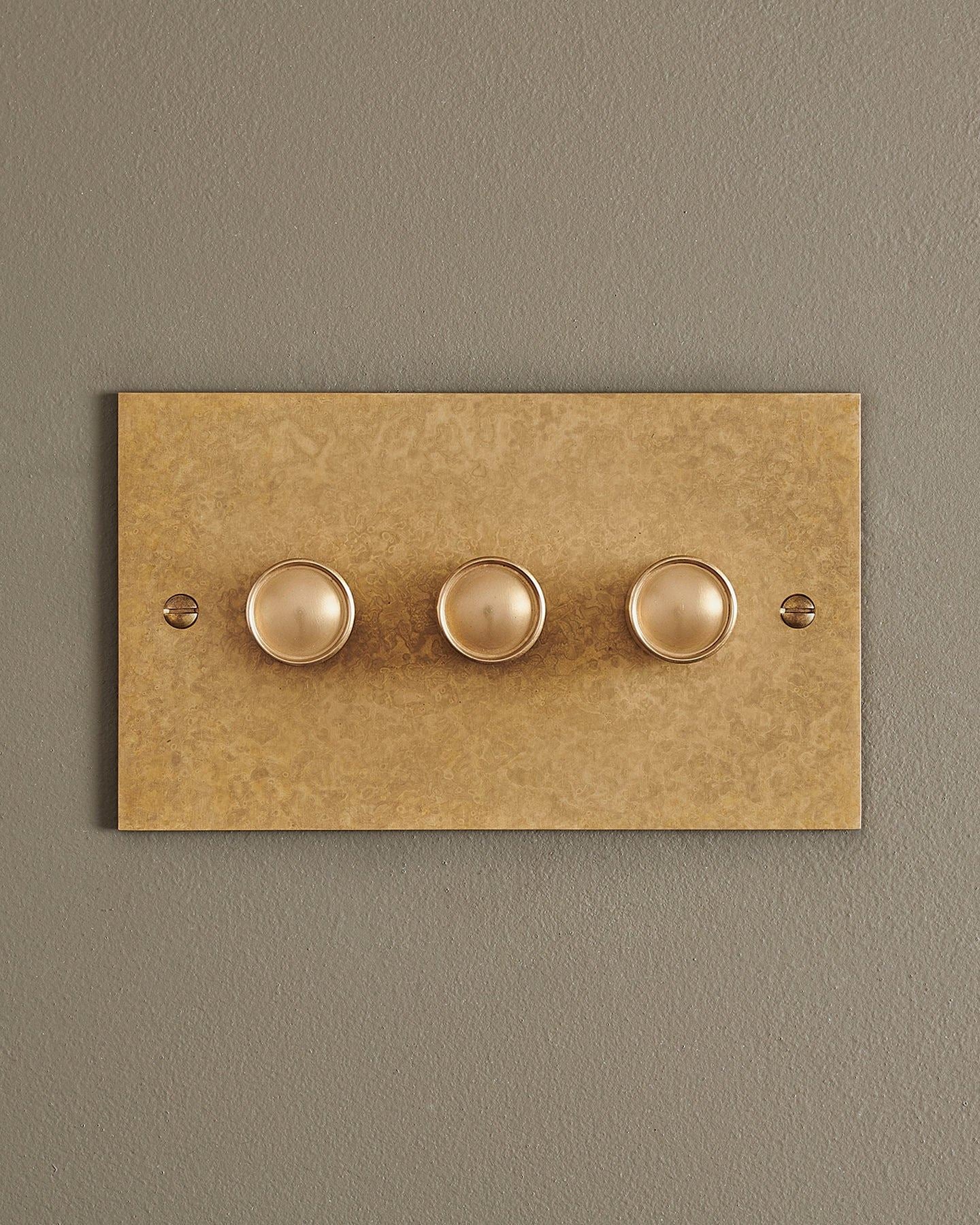 A straight-on view of a 3 gang classic dimmer switch in a mottled aged brass finish.