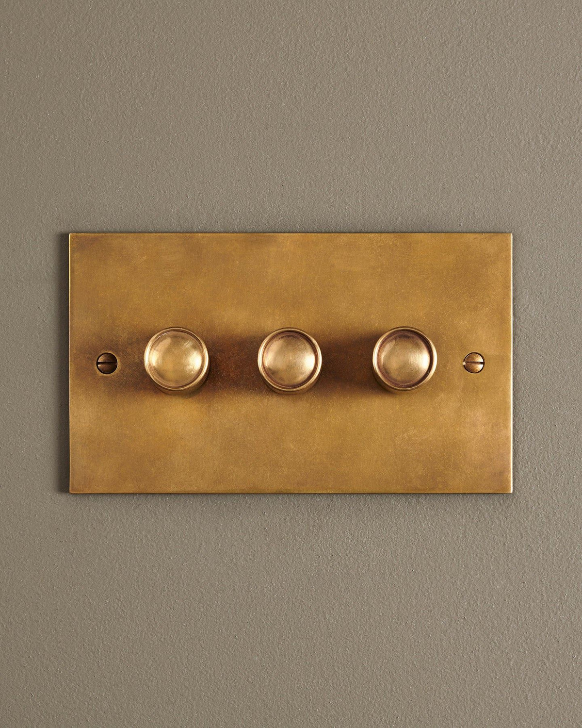 A straight-on view of a 3 gang classic dimmer switch in a warm burnished brass finish. TEST