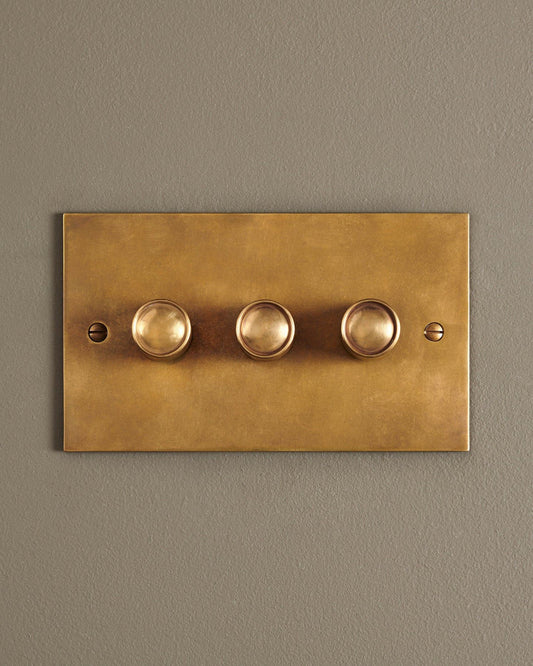A straight-on view of a 3 gang classic dimmer switch in a warm burnished brass finish.