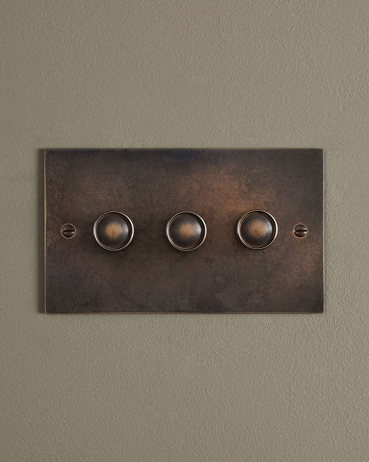 A straight-on view of a 3 gang classic dimmer switch in a dark oxidised brass finish. TEST